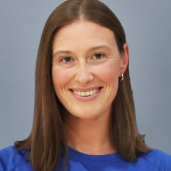 Smiling woman with shoulder-length brown hair in a blue shirt, facing the camera against a gray background.
