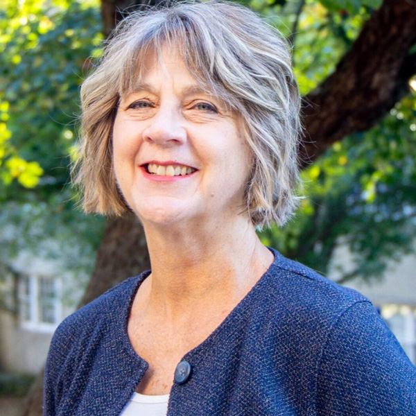 Smiling middle-aged woman with short gray hair outdoors, wearing a blue textured jacket.
