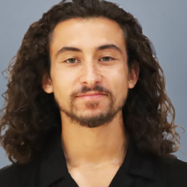 Head-and-shoulders portrait of a man with long curly hair and light beard, wearing a black shirt.