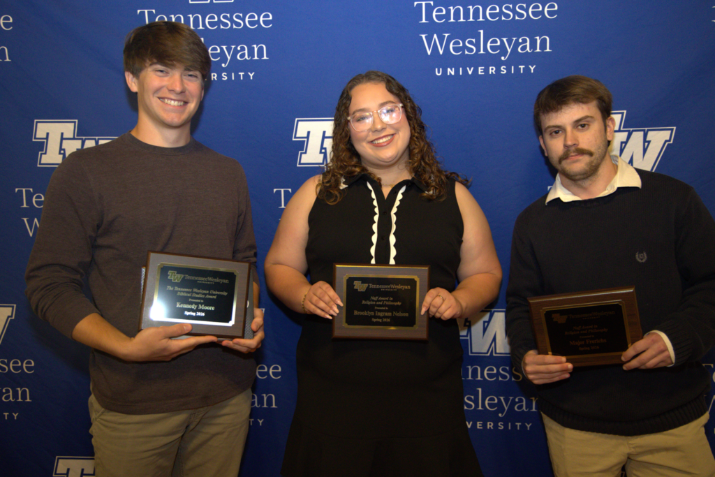 Three young adults pose with awards in front of a Tennessee Wesleyan backdrop at an awards event.