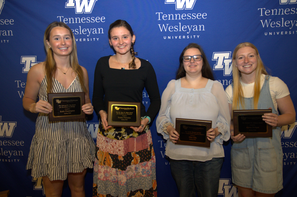 Four young women stand side by side, each holding an award plaque in front of a Tennessee Wesleyan backdrop.