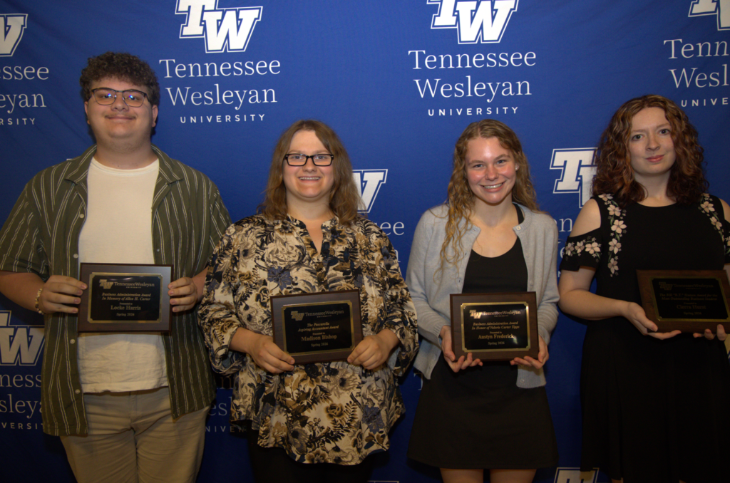 Four students standing side by side, each holding an award plaque, in front of a Tennessee Wesleyan University blue backdrop.