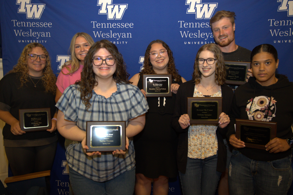 Group of eight students posing with awards in front of a Tennessee Wesleyan backdrop at an awards ceremony.
