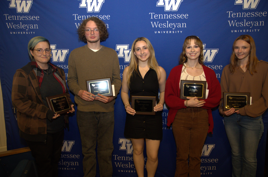 Five students pose with awards in front of a Tennessee Wesleyan University backdrop filled with TWU logos.