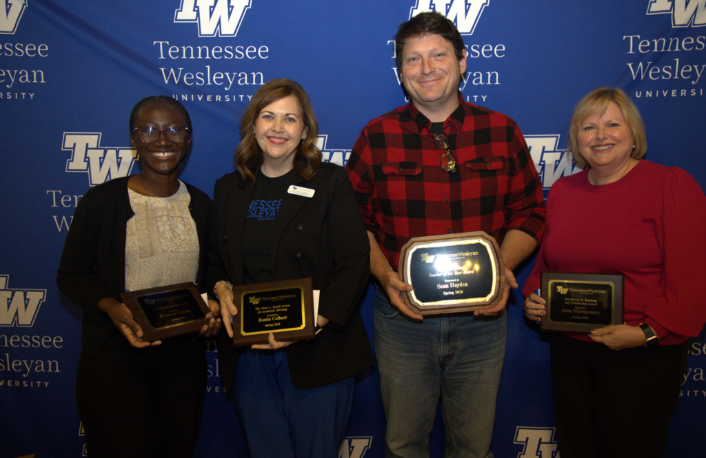Group of four award recipients posing in front of a Tennessee Wesleyan backdrop, each holding a plaque or trophy.