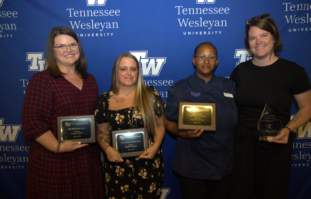 Four women pose with awards in front of a Tennessee Wesleyan University backdrop, each holding a plaque or trophy.