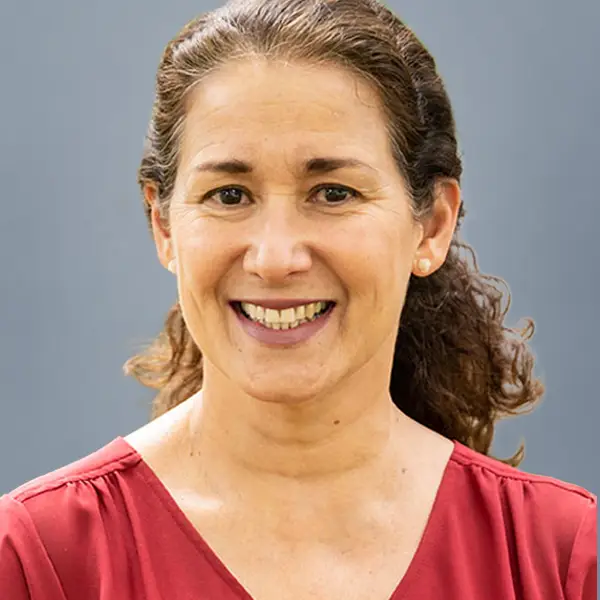 Smiling woman with brown hair tied back, wearing a red blouse, against a gray background (staff headshot).