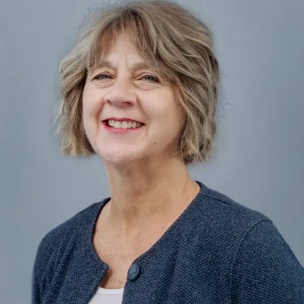 Smiling woman in a blue blazer posing for a professional headshot against a gray background.