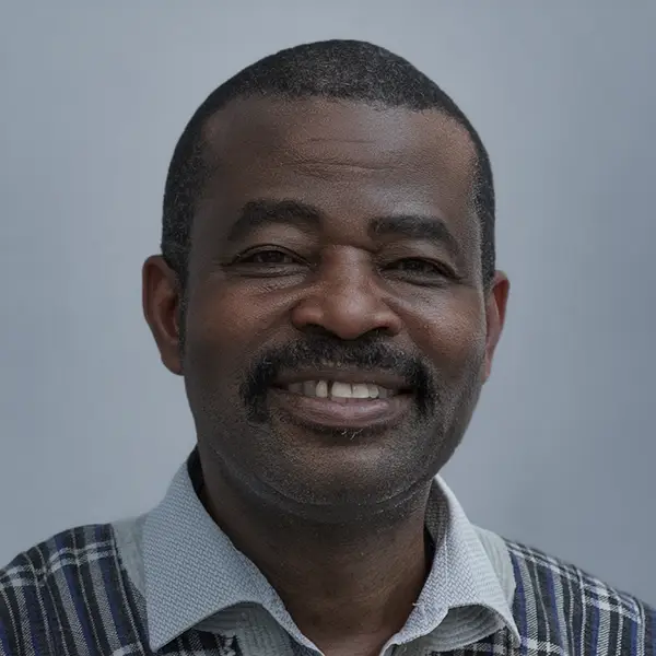 Smiling man with short hair and mustache wearing a light collared shirt and plaid sweater against a gray backdrop.