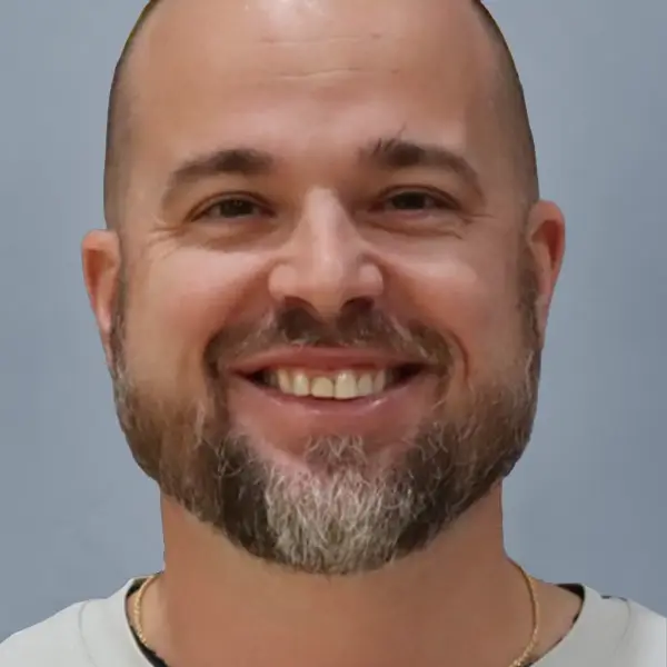 Smiling man with a trimmed beard and short hair against a gray background.