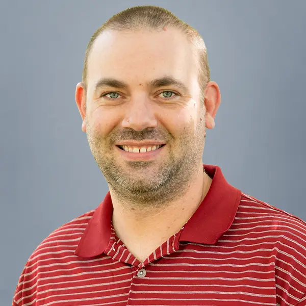 Smiling man wearing a red striped polo shirt against a gray backdrop (head-and-shoulders portrait).