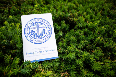 Tennessee Wesleyan University commencement program resting on green shrubbery; page shows 'Spring Commencement'.