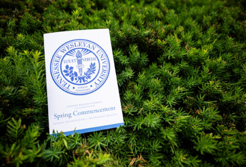Tennessee Wesleyan University commencement program resting on green shrubbery; page shows 'Spring Commencement'.