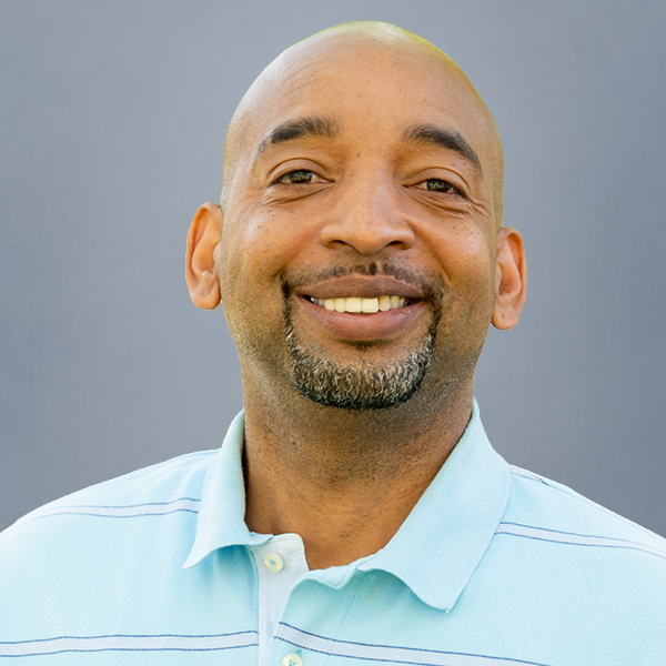 Smiling man in a light blue polo shirt posing for a headshot against a gray background, suitable for a professional profile page.