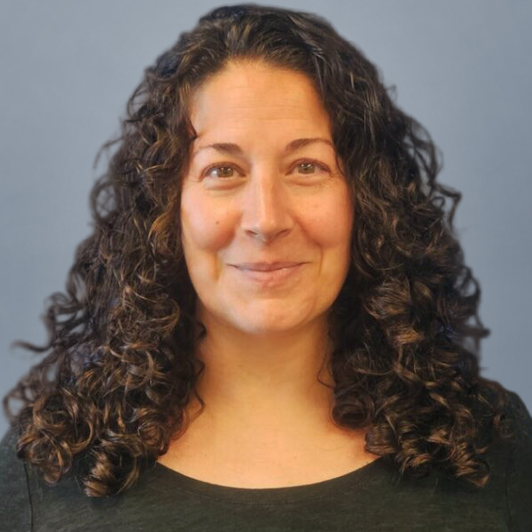 Portrait of a smiling woman with shoulder-length curly brown hair against a blue background.