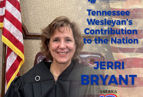 Portrait of a woman in a black judge's robe with an American flag and a Tennessee Wesleyan banner in the background.