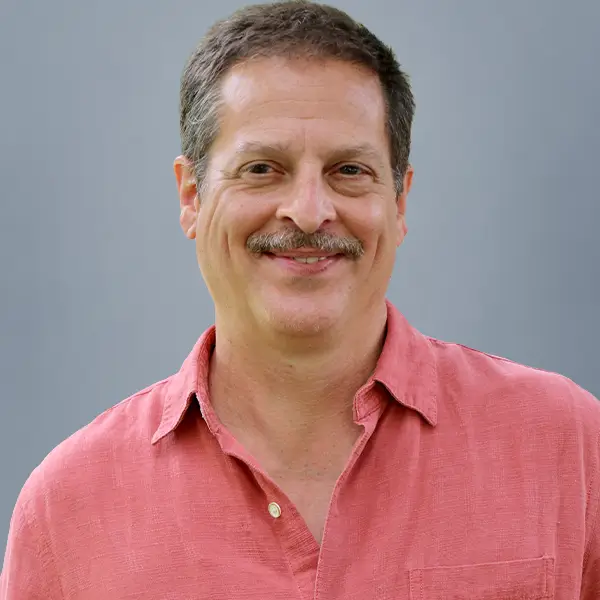 Smiling middle-aged man with short brown hair and a mustache, wearing a pink button-down shirt against a gray background.