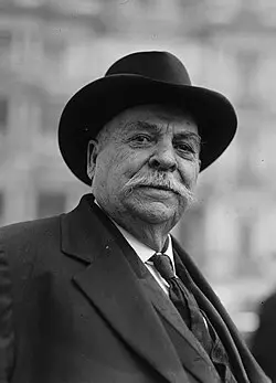 Black-and-white portrait of an older man in a suit and fedora, looking at the camera with a mustache.