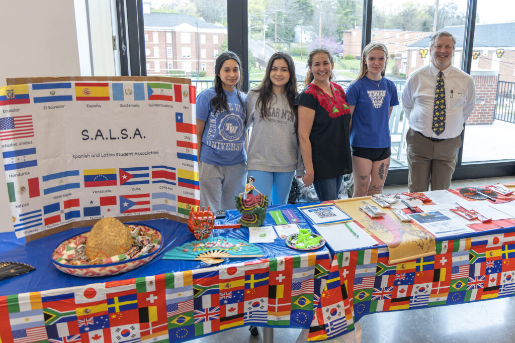 Five people stand beside a table draped in a flag-themed cloth, next to a large S.A.L.S.A. banner for the Spanish and Latino Student Association.