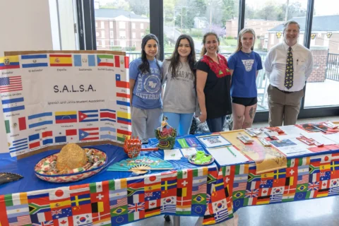 Five people stand beside a table draped in a flag-themed cloth, next to a large S.A.L.S.A. banner for the Spanish and Latino Student Association.