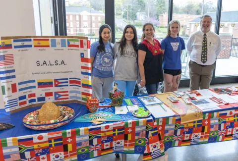 Five people stand beside a table draped in a flag-themed cloth, next to a large S.A.L.S.A. banner for the Spanish and Latino Student Association.