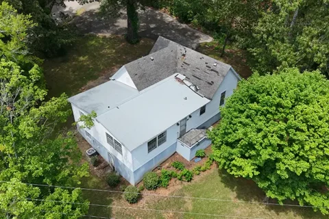 Aerial view of a white two-story house with a gray roof, surrounded by green trees and a grassy yard.