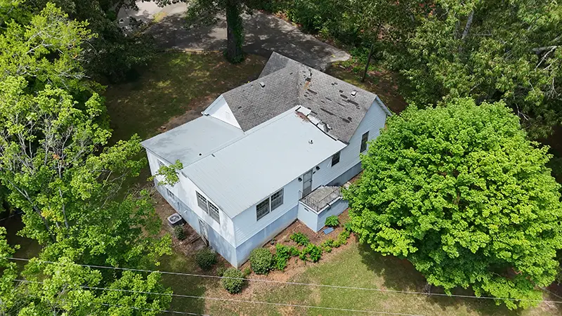Aerial view of a white two-story house with a gray roof, surrounded by green trees and a grassy yard.