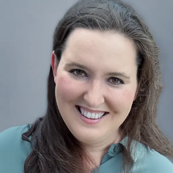 Portrait of a smiling woman with long brown hair wearing a teal shirt, against a neutral gray background