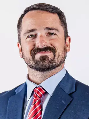 | Tennessee Wesleyan University Portrait of a man in a blue suit and red striped tie, smiling at the camera.